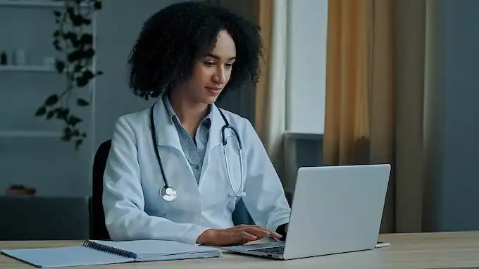Female doctor working on a laptop for telehealth or online medical consultation.